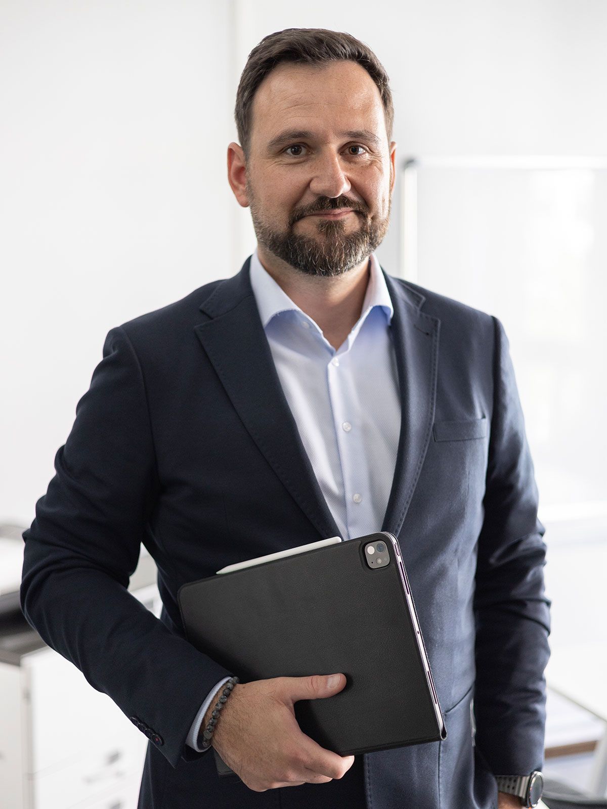 Oliver Bajunovic steht im Büro, ein Tablet unter dem Arm